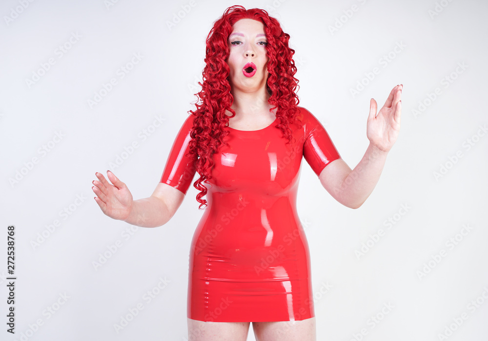 Photo Stock real doll woman wearing red latex rubber dress and posing on white studio background alone. curvy plus size adult girl standing as a plastic sex toy alone. | Adobe Stock Photo Stock real doll woman wearing red latex rubber dress and posing on white studio background alone. curvy plus size adult girl standing as a plastic sex toy alone. | Adobe Stock