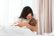 © New Africa - Mother with her adorable baby sitting on bed indoors