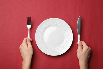 Wall Mural - Woman with fork, knife and empty plate on color background, top view