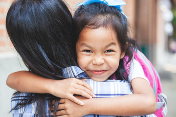 Wall Mural - Back to school. Cute asian pupil girl with backpack hugging her mother with happiness after back from school