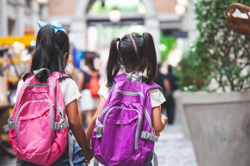 Wall Mural - Back to school. Two cute asian child girls with school bag holding hand and walk together in the school