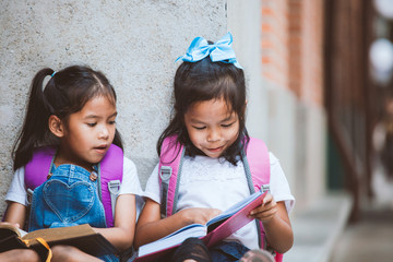 Wall Mural - Back to school. Two cute asian pupil girls reading a book  together in the school with fun and happiness