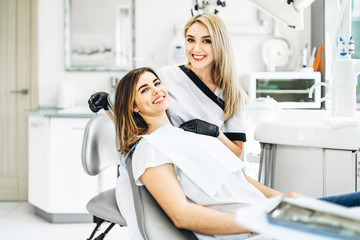 Wall Mural - Pretty young female dentist making examination and treatment for young female patient in dental clinic.