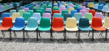 Long Rows Of Empty Colorful  Plastic Chairs Geometrically Arranged Under The Sun. Texture And Background. Copy Space..	