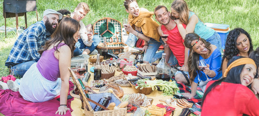 Group of friends making picnic in nature park outdoor - Young trendy people drinking wine and laughing together outside - Focus on man with red t-shirt - Youth, summer and friendship concept