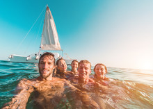 Happy Friends Taking A Selfie With Action Cam Inside The Ocean With Sail Boat In Background - Young People Having Fun Swimming In The Sea - Focus On Left Man Face - Travel And Youth Concept