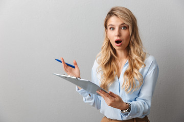 Wall Mural - Shocked young pretty blonde business woman posing isolated grey wall background holding clipboard.