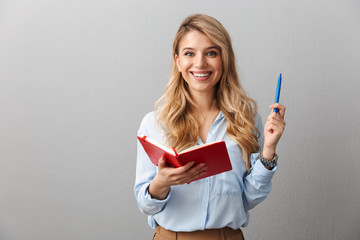 Sticker - Happy young pretty blonde business woman posing isolated grey wall background writing notes in notebook.