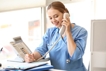 Canvas Print - Young medical assistant talking by phone in clinic