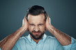 © G-Stock Faces - Problems. Frustrated young man covering ears with hands while standing against grey background