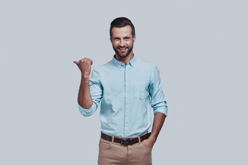 Solution is here. Handsome young man pointing copy space and looking at camera while standing against grey background