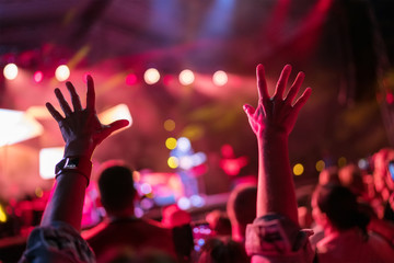 Young teenager girl raised up two hands supporting favorite popular band on the night concert. Crowdy entertainment with light and laser show.