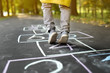 Closeup of little boy's legs and hopscotch drawn on asphalt. Child playing hopscotch game on playground outdoors on a sunny day.