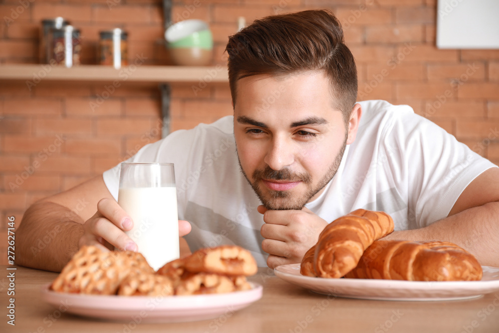Handsome man drinking tasty milk with bakery in kitchen at home