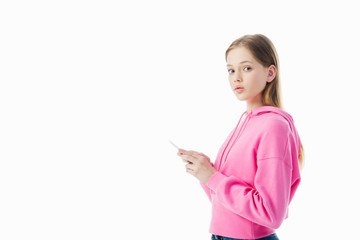 Wall Mural - teenage girl in pink hoodie using smartphone and looking at camera isolated on white