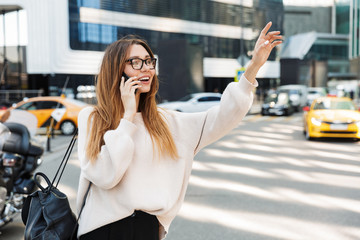 Poster - Photo of nice caucasian woman talking on cellphone with raised her arm while walking in big city street