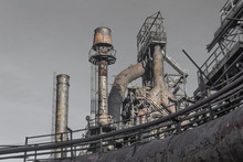 Exterior View Of Steel Mill Complex With Pipes And Smokestacks Against A Gray Sky, Horizontal Aspect