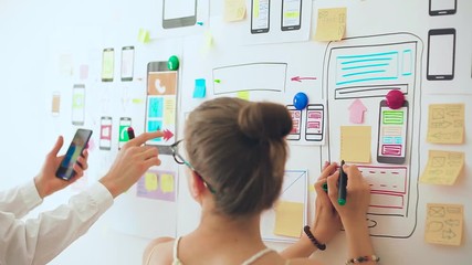 Aufkleber - Designers is developing a web application for mobile phones. Woman draws a mockup of interface to smartphone. User experience. 