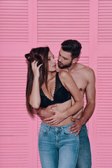 Wall Mural - Appreciating every minute together. Beautiful young couple embracing while standing against pink background