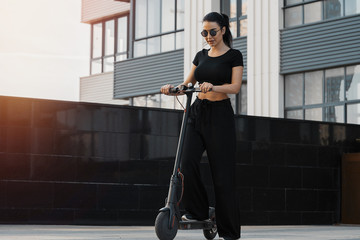 Sticker - Young attractive woman riding electrick kick scooter at modern cityscape.