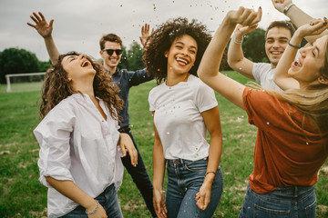 group of five friends having fun at the park - millennials dancing in a meadow among confetti thrown