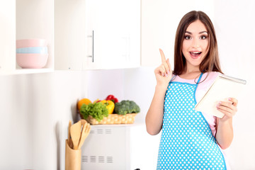 Wall Mural - Young woman with notepad cooking dinner in the kitchen