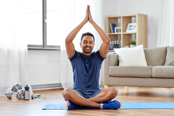 Wall Mural - fitness, meditation and healthy lifestyle concept - indian man meditating in lotus pose on exercise mat at home