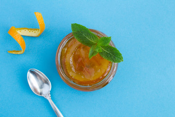 Wall Mural - Homemade orange marmalade in the glass jar on the blue background.Closeup.Top view.Copy space.