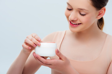 Wall Mural - happy teenage girl holding cosmetic cream isolated on grey