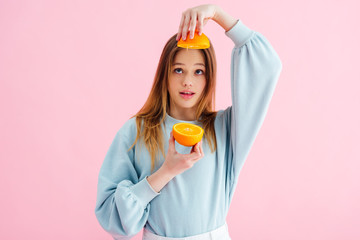 Wall Mural - pretty teenage girl looking at orange halves isolated on pink