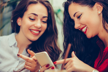 Two young women sharing social media in a smart phone at cafe