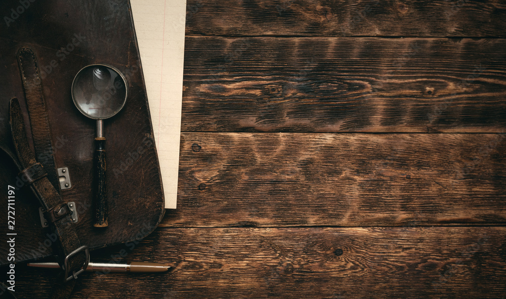 Leather bag and a blank letter with a pen a magnifying glass on brown ...