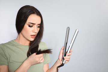 Wall Mural - Emotional woman with hair iron on grey background. Space for text