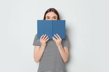 Sticker - Young woman hiding behind book on white background, space for text. Reading activity