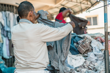 Thai old senior man choosing second hand cloth on street. Thai people lifestyle.