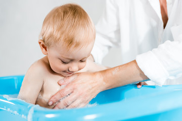 cropped view of woman washing cute toddler child in baby bathtub