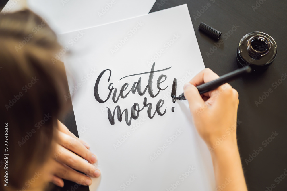 Creat more. Calligrapher Young Woman writes phrase on white paper. Inscribing ornamental decorated letters. Calligraphy, graphic design, lettering, handwriting, creation concept - obrazy, fototapety, plakaty 
