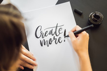 Creat More. Calligrapher Young Woman Writes Phrase On White Paper. Inscribing Ornamental Decorated Letters. Calligraphy, Graphic Design, Lettering, Handwriting, Creation Concept