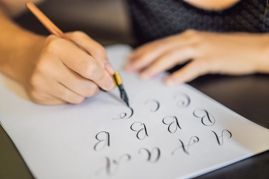 Calligrapher Young Woman writes phrase on white paper. Inscribing ornamental decorated letters. Calligraphy, graphic design, lettering, handwriting, creation concept