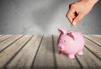 Poster - Hand putting coin to piggy bank on blue background