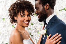 Cheerful African American Bride Hugging Handsome Bridegroom Near Flowers