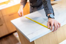Male Hand Designer Using Tape Measure For Measuring White Granite Countertops On Modern Kitchen Counter In Showroom. Shopping Furniture Material For Home Improvement. Interior Design Concept