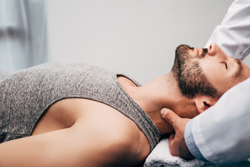 chiropractor massaging neck of man lying on towel in hospital