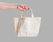 Tote Bag Canvas White Cotton Fabric Cloth For Eco Shoulder Shopping Sack Mockup Blank Template Isolated On Grey Background (clipping Path) With Woman’s Hand Handling Handle Straps
