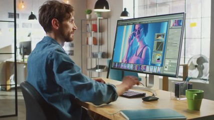 Poster - Male Digital Editor in Jeans Shirt Works in Photo Editing Software on His Personal Computer with Big Display. He Works in Cool Office Loft. Other Female Creative Colleague Walks in the Background.