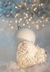 Wall Mural - New year or Christmas decoration. Glass white heart and a ball with pearls on a snow. Blurred background of glittering bokeh.