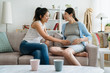 asian young japanese woman visit pregnant friend at home sitting on couch in cozy living room. two ladies with future motherhood relax on sofa while girl one hand touching belly feeling baby moving