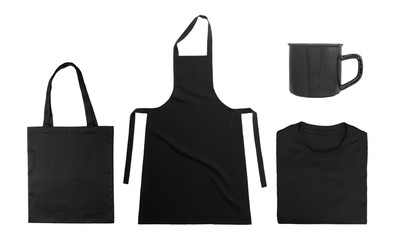 Wall Mural - Collection of black objects isolated on white background. Black cotton bag, black folded t-shirt, kitchen apron, metal mug. Flat lay. Top view