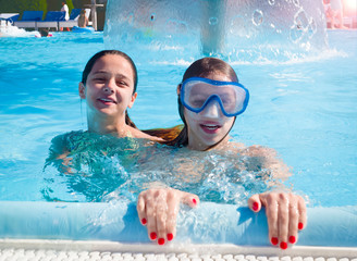 Two happy children playing on the swimming pool in aqua park at the day time. People having fun outdoors. Concept of friendly family and summer vacation.