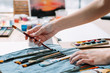© golubovy - Professional artist kit. Closeup of painter hands choosing brush for working on new picture. Blur studio background.